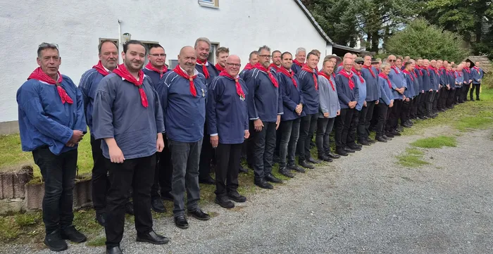 Eine lange Reihe von Bauernschützen in blauen Hemden und roten Halstüchern steht vor einem weißen Gebäude.