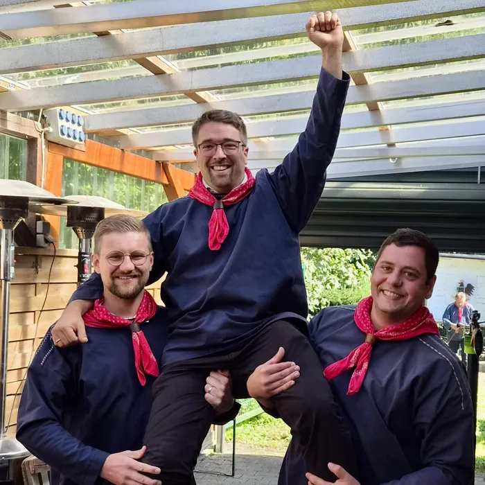 Tobias Sieper wird von zwei Männern in blauen Hemden und roten Halstüchern hochgehoben, während er den Arm mit geballter Faust hebt.