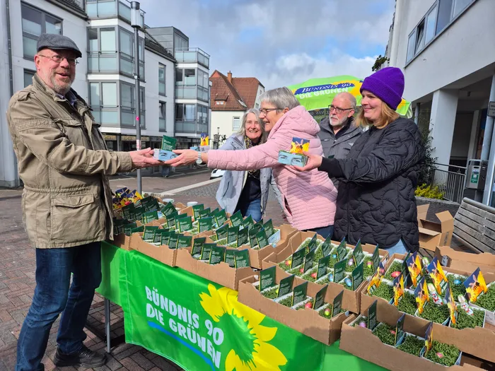Ein Mann übergibt einer Frau an einem Stand mit Kresse und Blumensamen der Partei Bündnis 90/Die Grünen eine kleine Schale mit Kresse.