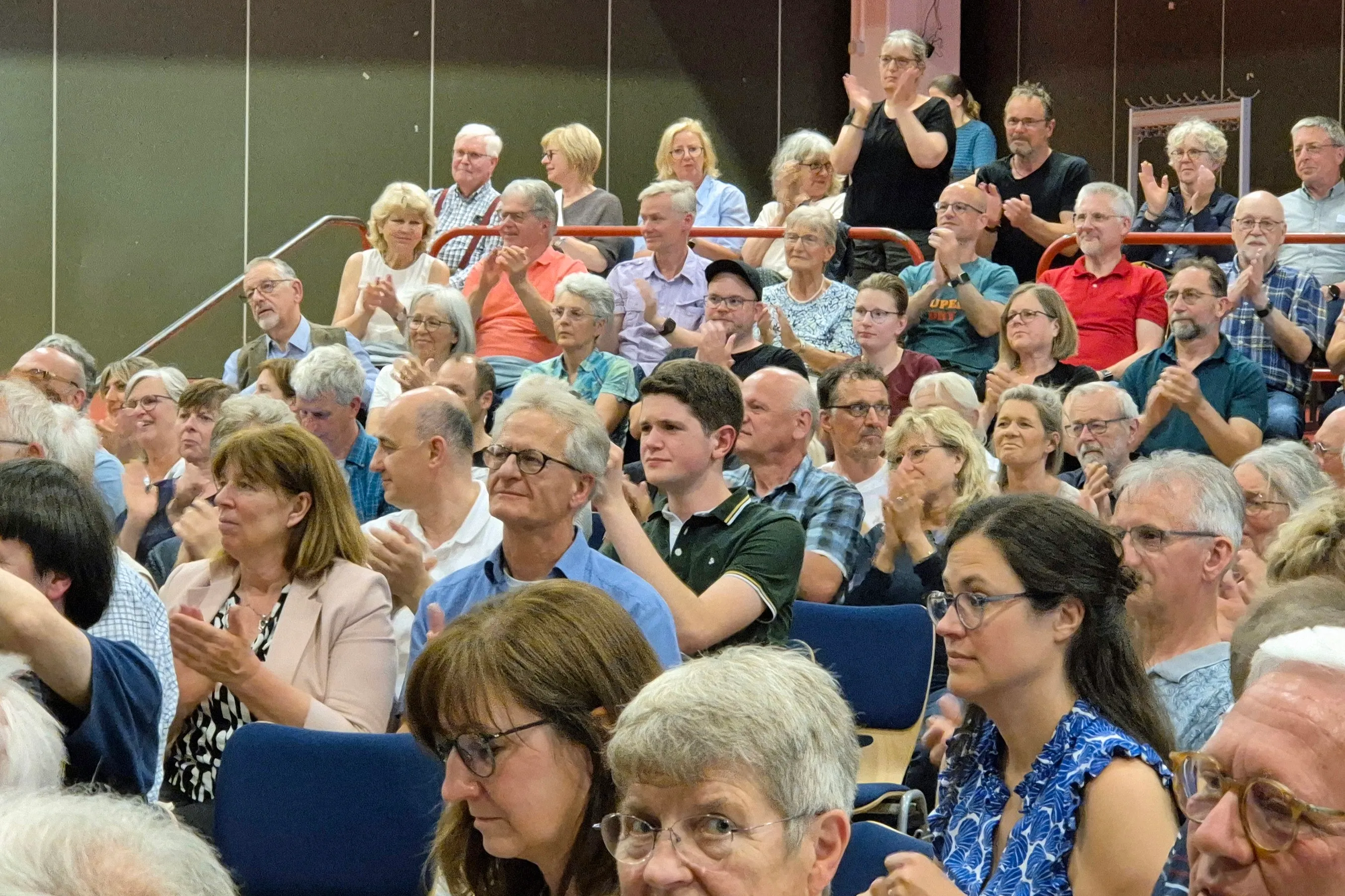 Zuschauer klatschen in einem voll besetzten Saal bei einer Kulturveranstaltung. Viele Menschen unterschiedlichen Alters sind zu sehen.