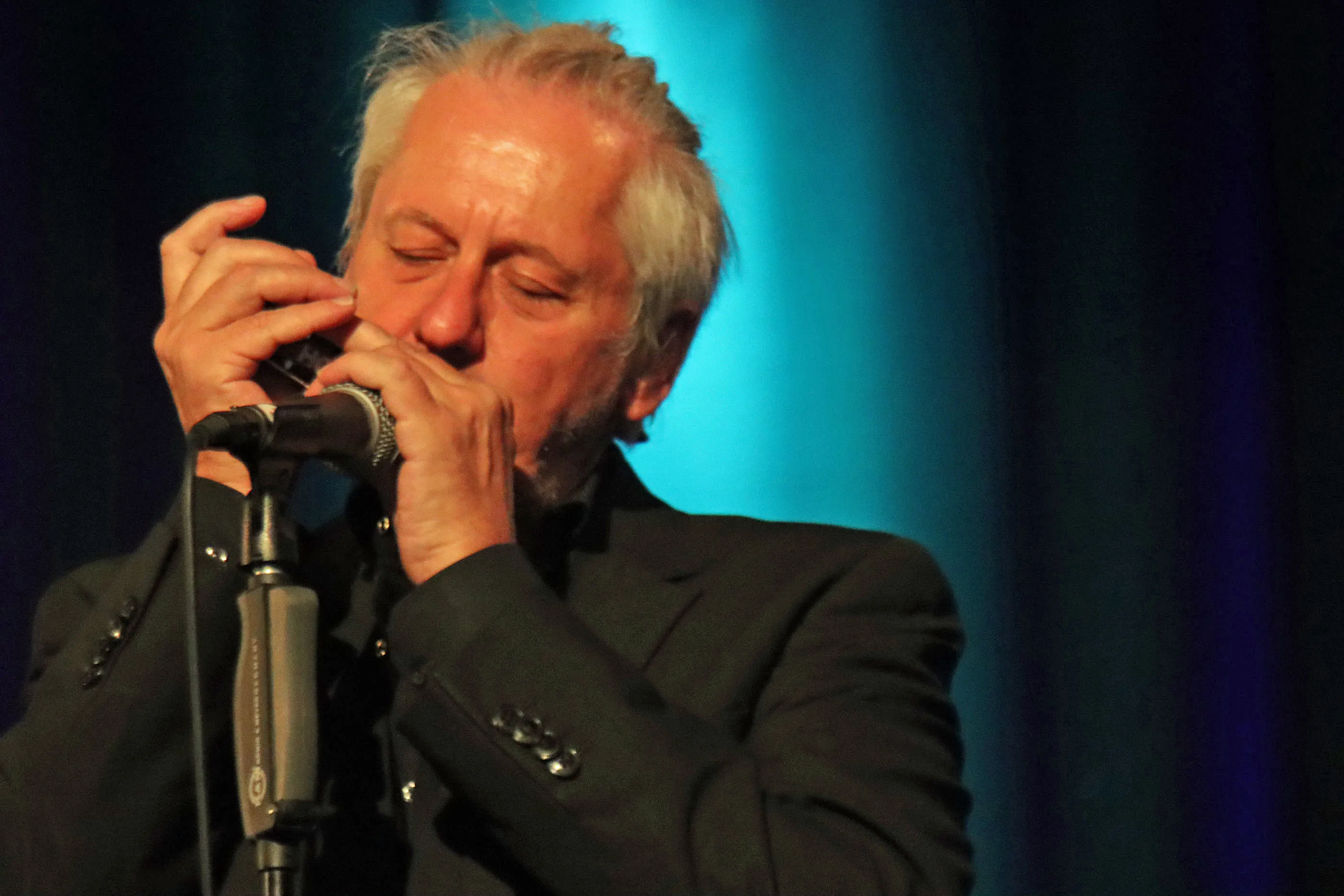 Marc Breitfelder spielt Mundharmonika in ein Mikrofon, während er den Blick geschlossen hat.