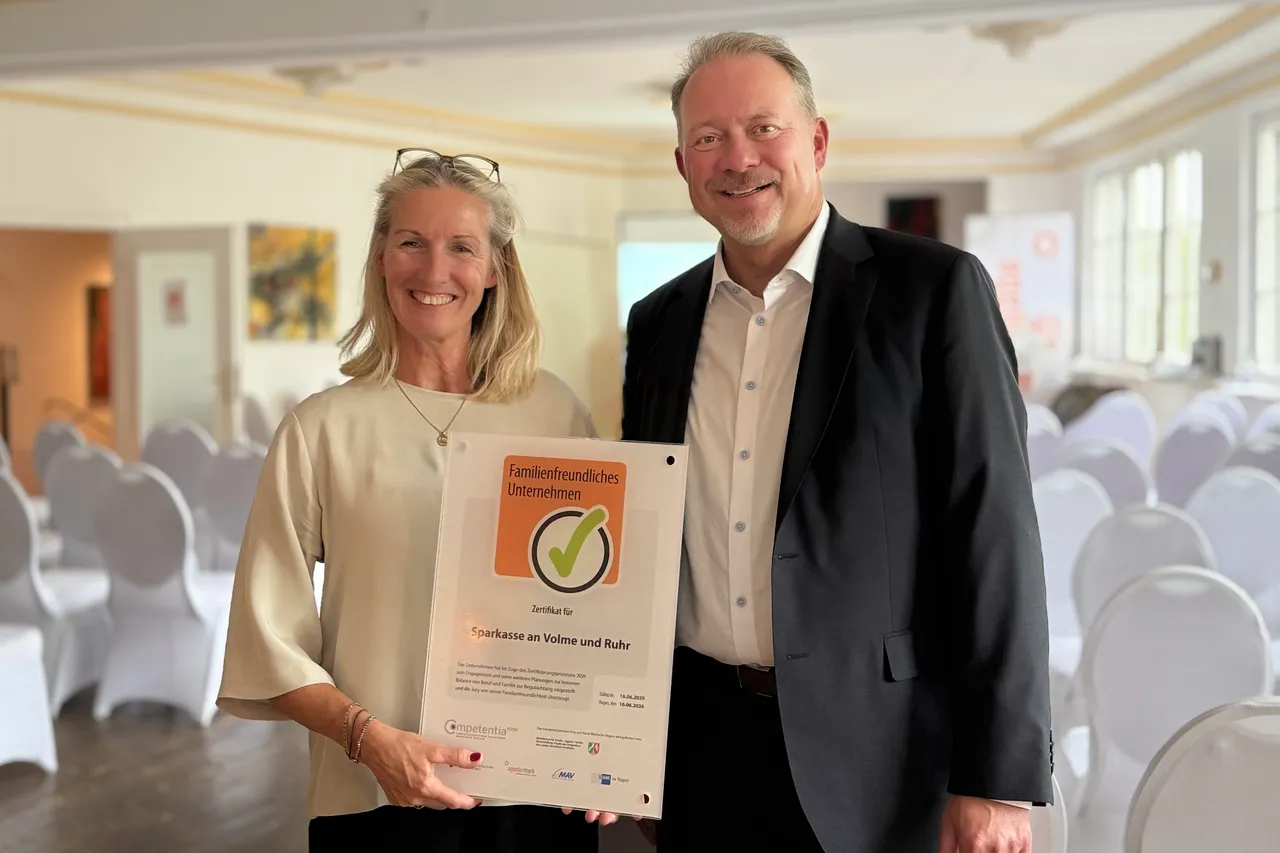 Zwei Personen, eine Frau und ein Mann, halten ein Zertifikat mit dem Titel „Familienfreundliches Unternehmen“ und dem Logo der Sparkasse an Volme und Ruhr. Die Frau hält das Zertifikat, während der Mann neben ihr steht und lächelt.