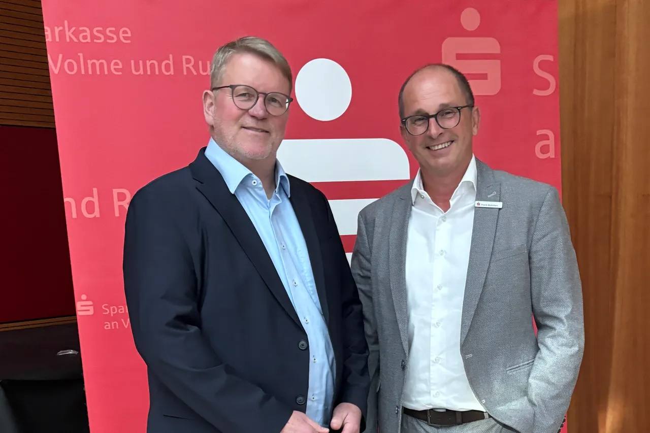 Zwei lächelnde Männer mit Brille im Anzug stehen vor rotem Hintergrund mit Sparkassen-Logo und Text. Links Jörg Klepper, rechts Frank Mohrherr.