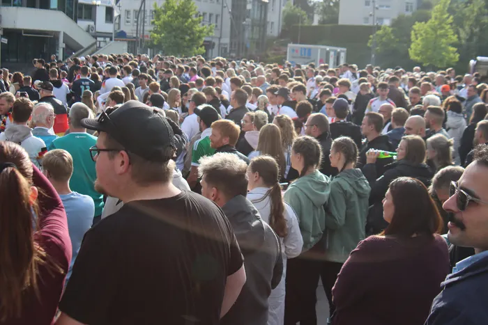 Große Menschenmenge beim Public Viewing eines Fußballspiels, viele schauen in eine Richtung. Jubelnde Gesichter und eine ausgelassene Stimmung sind erkennbar.