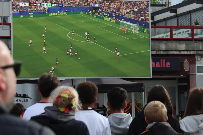 Fußballspiel Deutschland gegen Curaçao auf einer Großbildleinwand während eines Public Viewings. Menschen schauen dem Spiel zu.