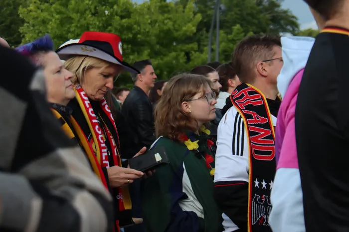 Zuschauer beim Public Viewing der Fußball-WM jubeln, viele tragen Deutschland-Schals und -Fahnen. Eine Frau schaut auf ihr Handy.