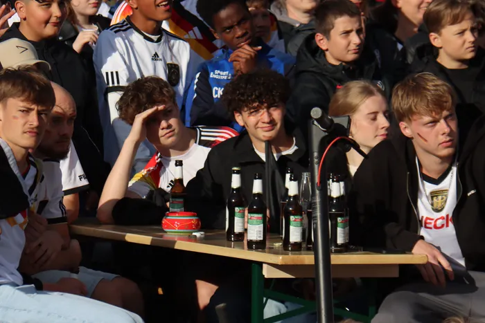 Junge Menschen feiern beim Public Viewing des Fußballspiels Deutschland gegen Curaçao. Auf einem Tisch vor ihnen stehen mehrere Bierflaschen.
