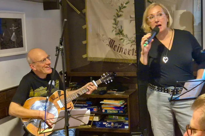 Achim Neubert spielt eine Resonatorgitarre, während Alexandra Middel in ein Mikrofon singt.