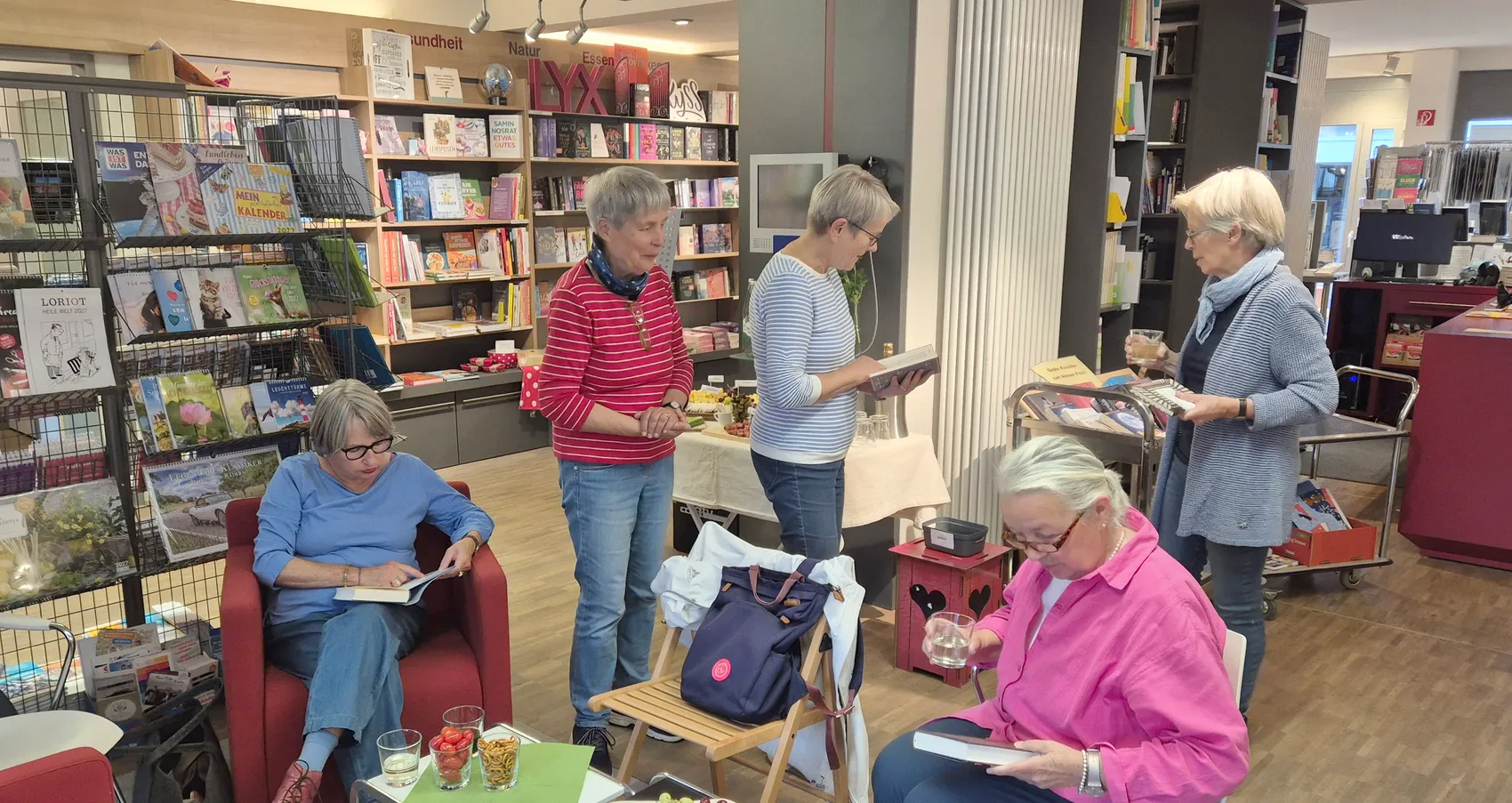 Mehrere Frauen lesen in einer Buchhandlung und halten teilweise Gläser mit Getränken.