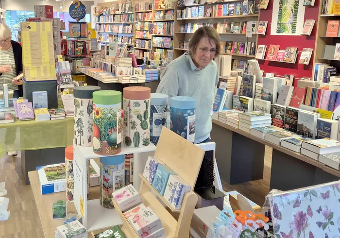 Eine Frau betrachtet in einer Buchhandlung verschiedene Bücher und bunte Dosen auf einem Display.