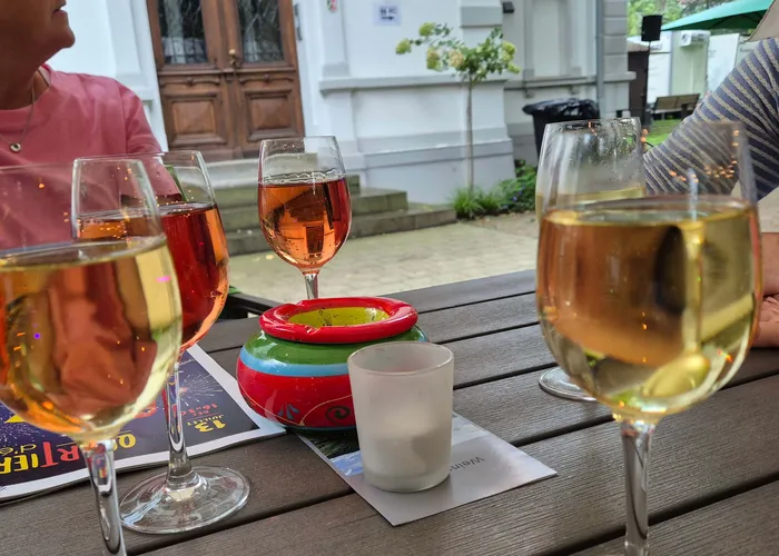 Gläser mit Weiß- und Roséwein auf einem Holztisch im Freien neben einer bunten Keramikschale.