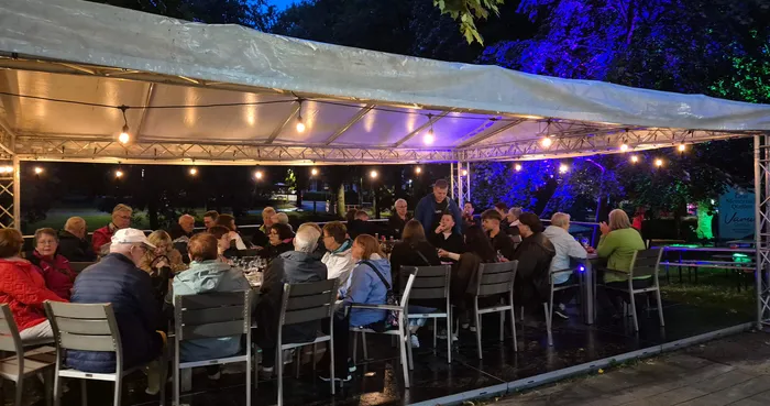 Menschen sitzen an Tischen unter einem mit Lichterketten beleuchteten Festzelt bei einem Weinfest.