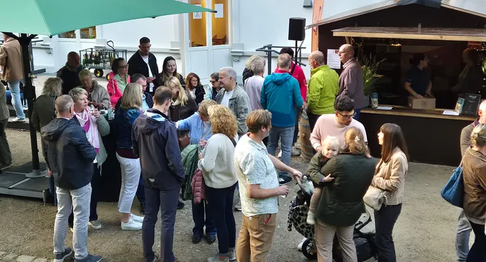 Menschen unterschiedlichen Alters unterhalten sich bei einem Weinfest im Volmepark vor einem kleinen Holzstand.