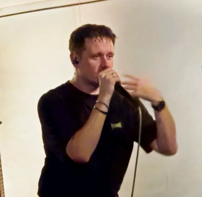 Chris Kramer singt in ein Mikrofon vor einem hellen Hintergrund.