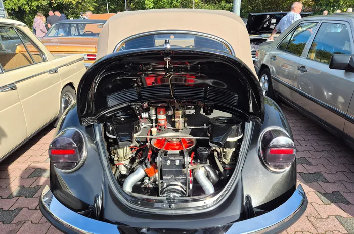 Blick in den offenen Motorraum eines dunkelgrauen Oldtimer-Cabrios mit roten Motorkomponenten.