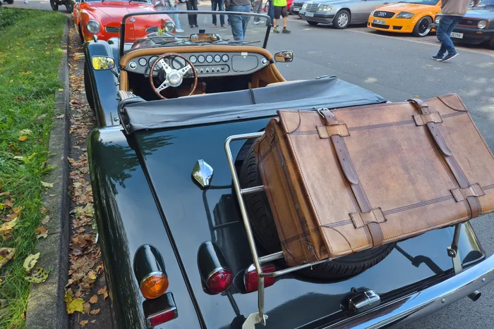 Ein dunkelgrünes Oldtimer-Cabriolet mit einem braunen Lederkoffer auf einem Gepäckträger am Heck.