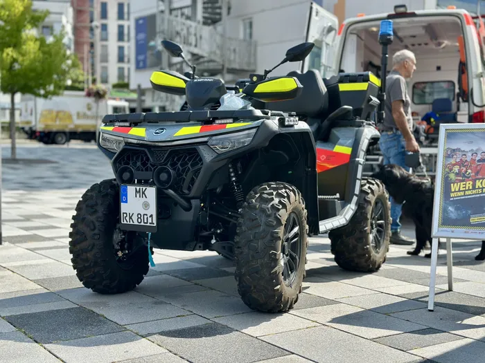 Ein Quad mit gelb-roten Warnmarkierungen steht auf einem gepflasterten Platz neben einem weißen Einsatzfahrzeug.