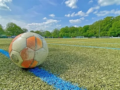 Fußball liegt auf dem Kunstrasenplatz, im Hintergrund Bäume und der Sportplatz Am Honsel in Lüdenscheid bei blauem Himmel. Die Aufnahme zeigt ein Spiel der Fußball-Kreismeisterschaft der Grundschulen.