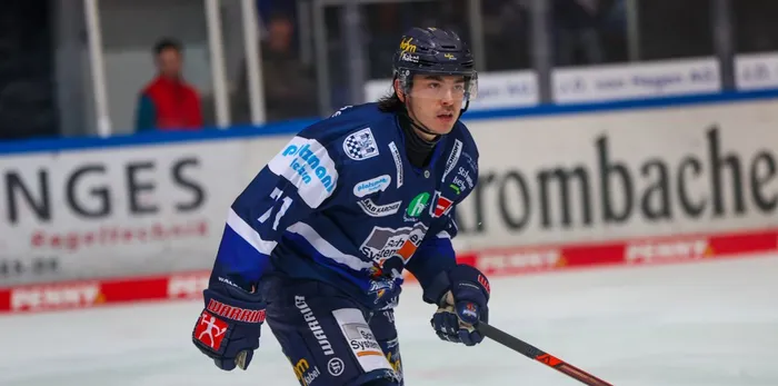 Eishockeyspieler Daniel Fischbuch in voller Ausrüstung mit Schläger auf dem Eis, während eines Spiels. Im Hintergrund sind Zuschauer und Werbebanden zu sehen.