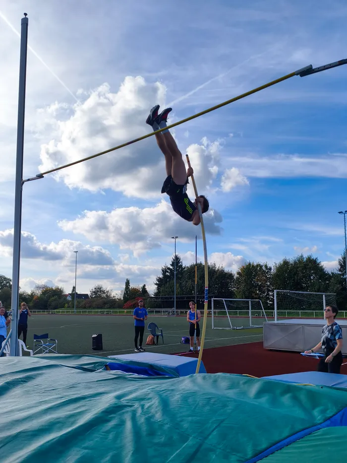 Ein Stabhochspringer überquert kopfüber die Latte bei einem Leichtathletikwettkampf unter blauem Himmel.