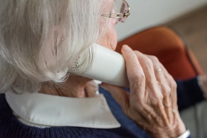 Eine ältere Person hält einen weißen Telefonhörer an ihr Ohr.