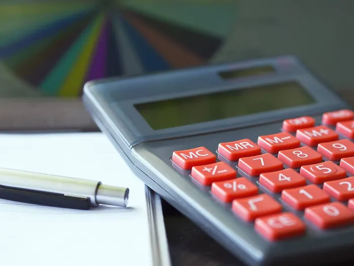 Taschenrechner mit orangefarbenen Tasten, ein Stift und ein weißes Blatt Papier.
