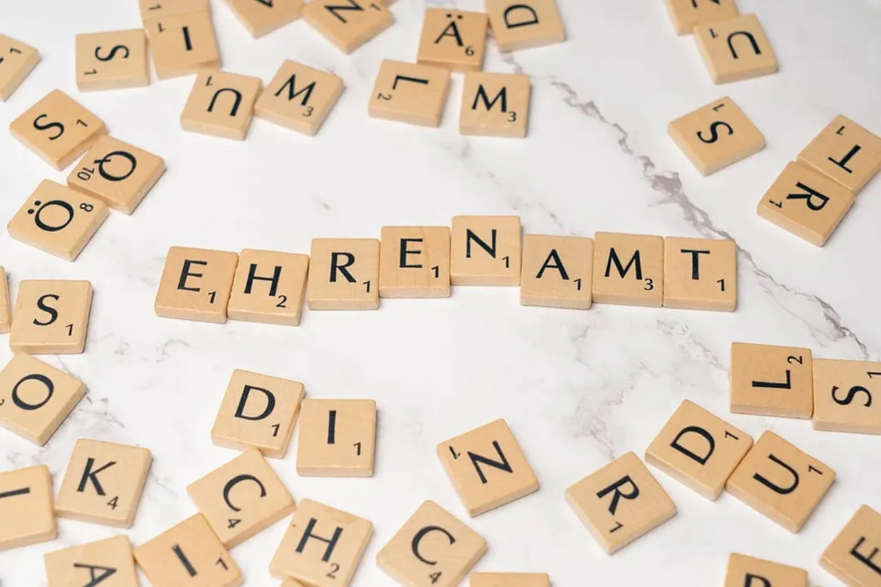 Holzbuchstaben, die das Wort „Ehrenamt“ auf einer hellen Marmoroberfläche bilden.