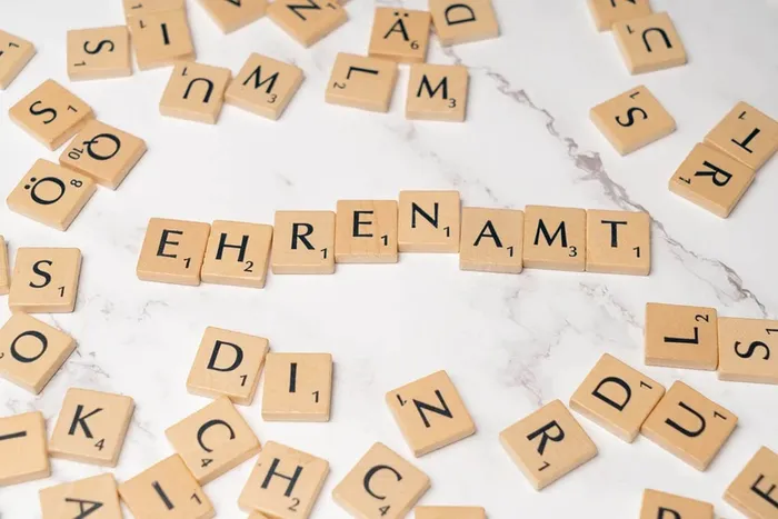 Holzbuchstaben, die das Wort „Ehrenamt“ auf einer hellen Marmoroberfläche bilden.