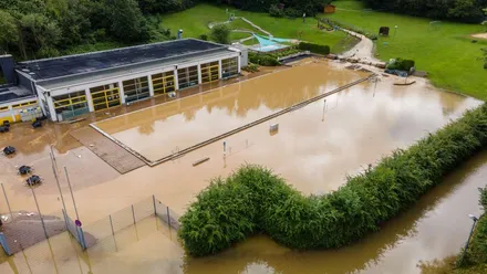 Das Gelände des Hallen- und Freibads in Altena-Dahle ist nach dem Hochwasser im Juli 2021 vollständig überflutet. Das Wasser bedeckt das Schwimmbecken und reicht bis an das Gebäude heran.