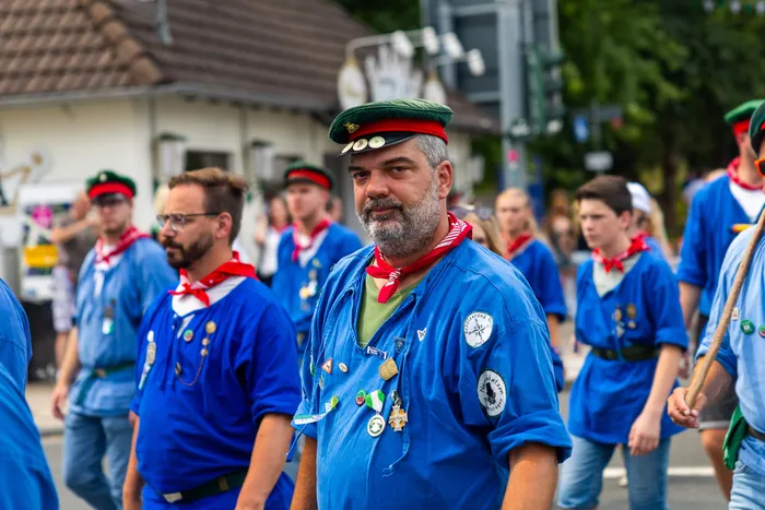 Stefan Schneider in blauer Uniform mit rotem Halstuch und grüner Kappe steht im Vordergrund vor weiteren Mitgliedern der Meinerzhagener Schützengilde.