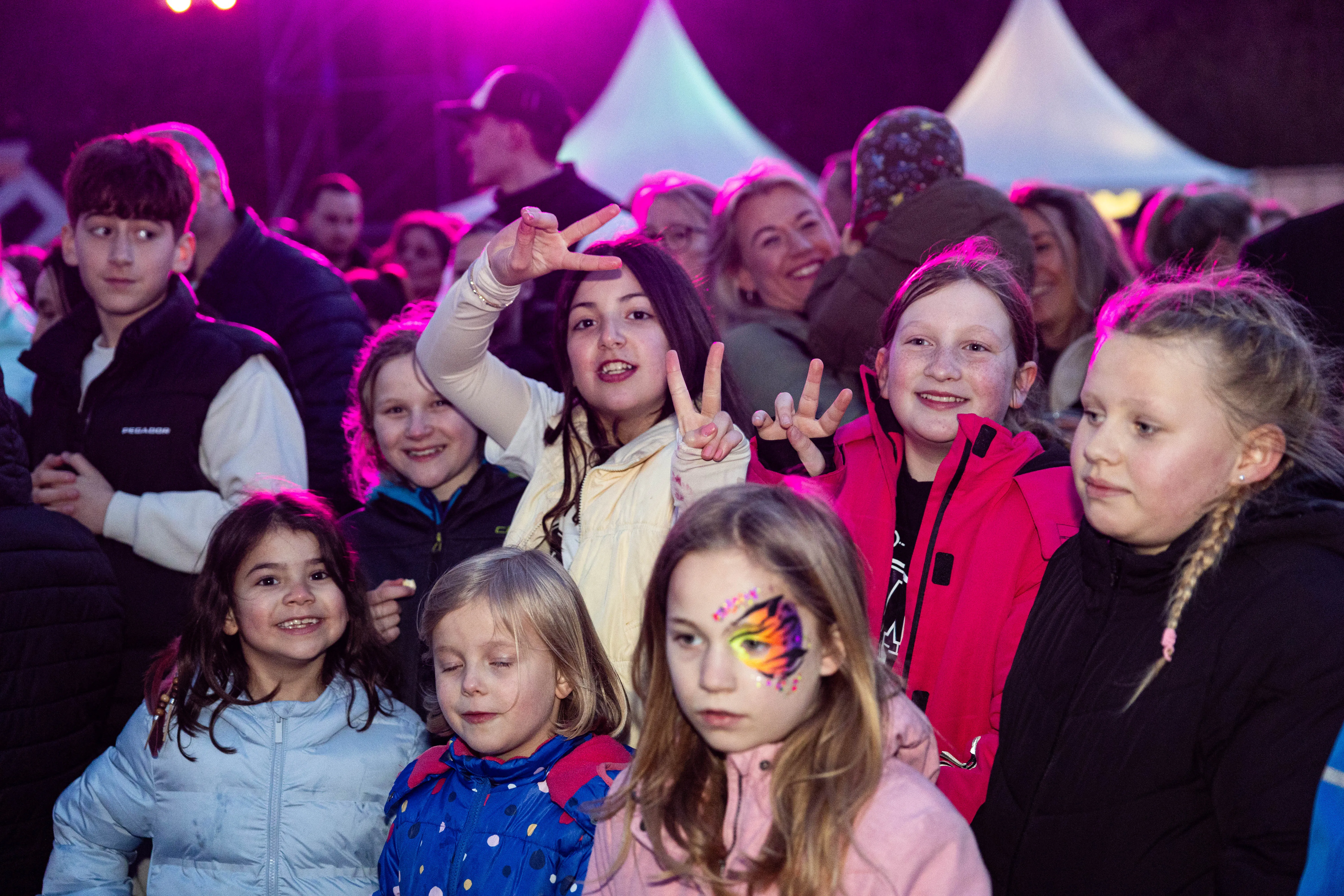Menschenmenge bei der Osterfeuer-Veranstaltung „Burn the Fox“ in Lüdenscheid, darunter viele Kinder und Jugendliche, die in die Kamera lächeln oder das Friedenszeichen zeigen.