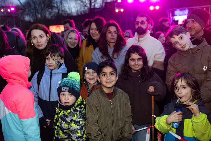 Eine Gruppe von Menschen, darunter viele Kinder, schaut in die Kamera. Im Hintergrund sind Lichter und weitere Menschen zu sehen.
