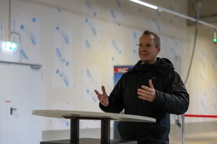 Alexander Tahl, Program Manager Technik Klimafreundliche Nutzfahrzeuge bei der NOW GmbH, gestikulierend vor einem Tisch in einem hellen Raum.