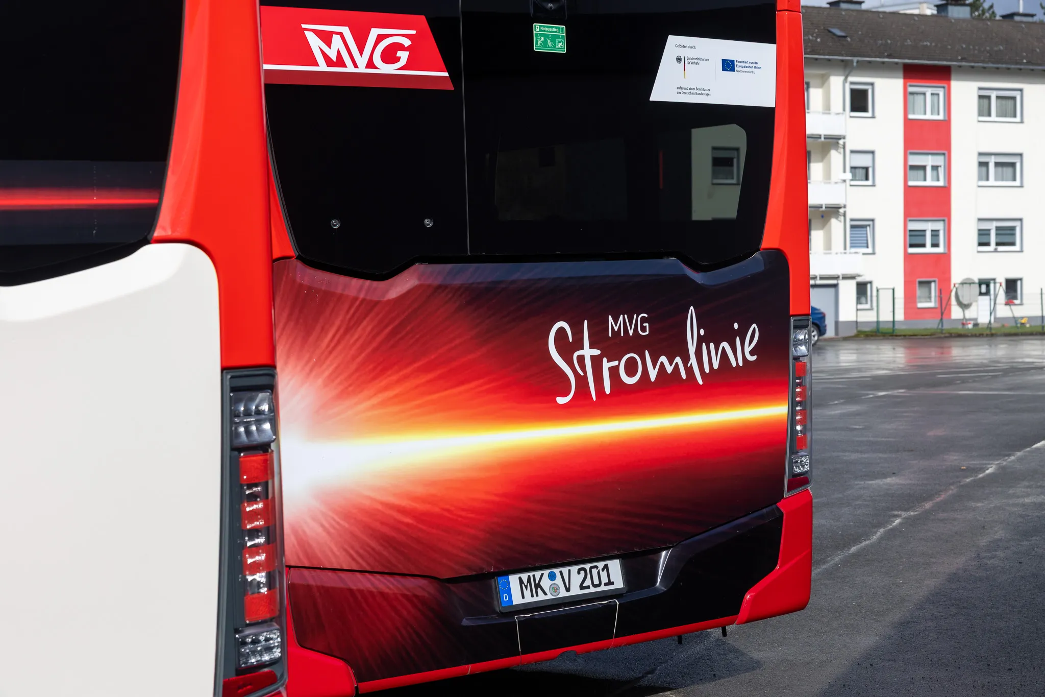 Heckansicht eines roten Elektrobusses der MVG mit dem Schriftzug „Stromlinie“ und dem Kennzeichen MK V 201 vor einem Wohngebäude.