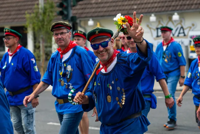 Stefan Schneider, der neue König der Meinerzhagener Schützengilde, lächelt und zeigt das Friedenszeichen mit einem blumengeschmückten Stab.
