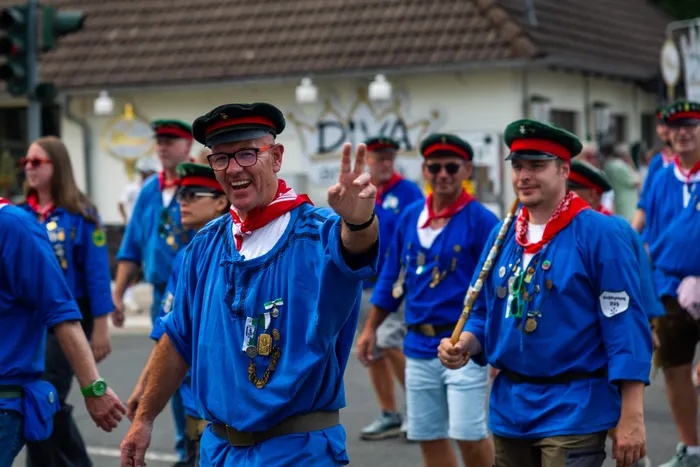 Ein Mann in blauer Uniform mit rotem Halstuch und Medaillen macht ein Friedenszeichen während der Parade der Schützengilde.