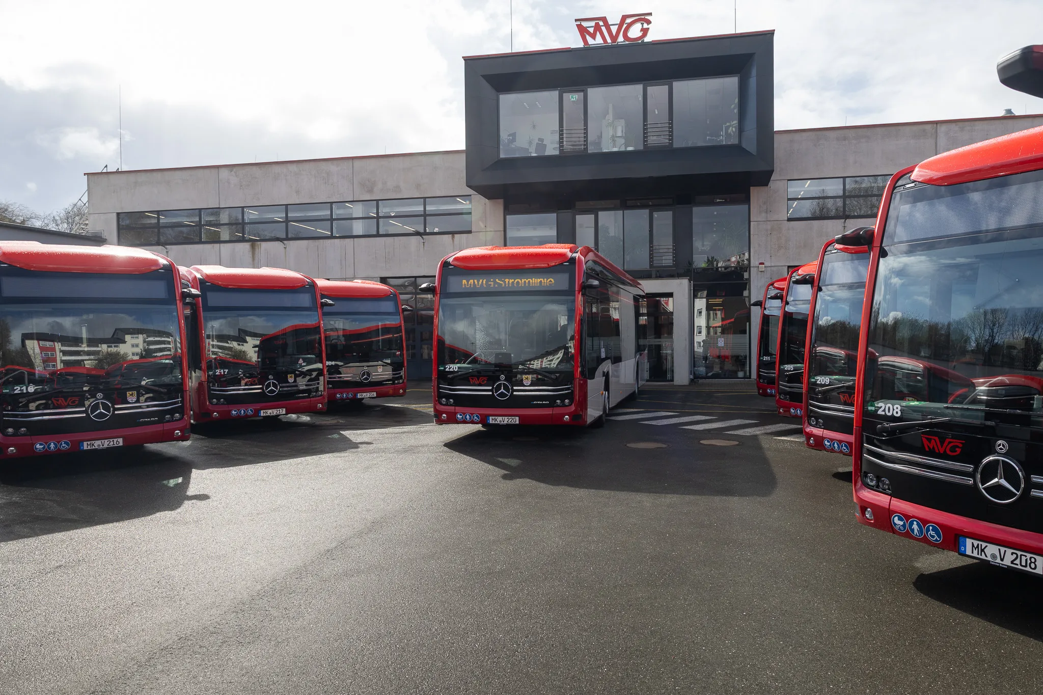 Vier rote Elektrobusse der Münchner Verkehrsgesellschaft (MVG) stehen vor einem modernen Gebäude mit dem MVG-Logo.