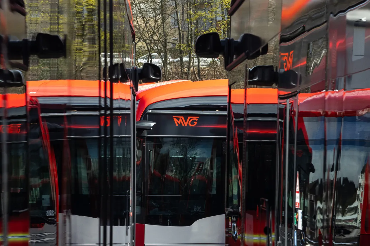 Mehrere rote Elektrobusse der Münchner Verkehrsgesellschaft (MVG) stehen nebeneinander, reflektiert in den glänzenden Seiten der Fahrzeuge.