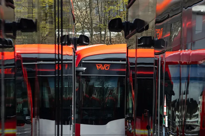 Mehrere rote Elektrobusse der Münchner Verkehrsgesellschaft (MVG) stehen nebeneinander, reflektiert in den glänzenden Seiten der Fahrzeuge.