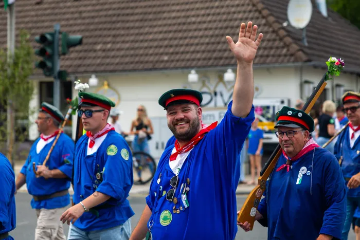 Stefan Schneider von der Meinerzhagener Schützengilde winkt in blauem Hemd, rotem Halstuch und grüner Kappe.