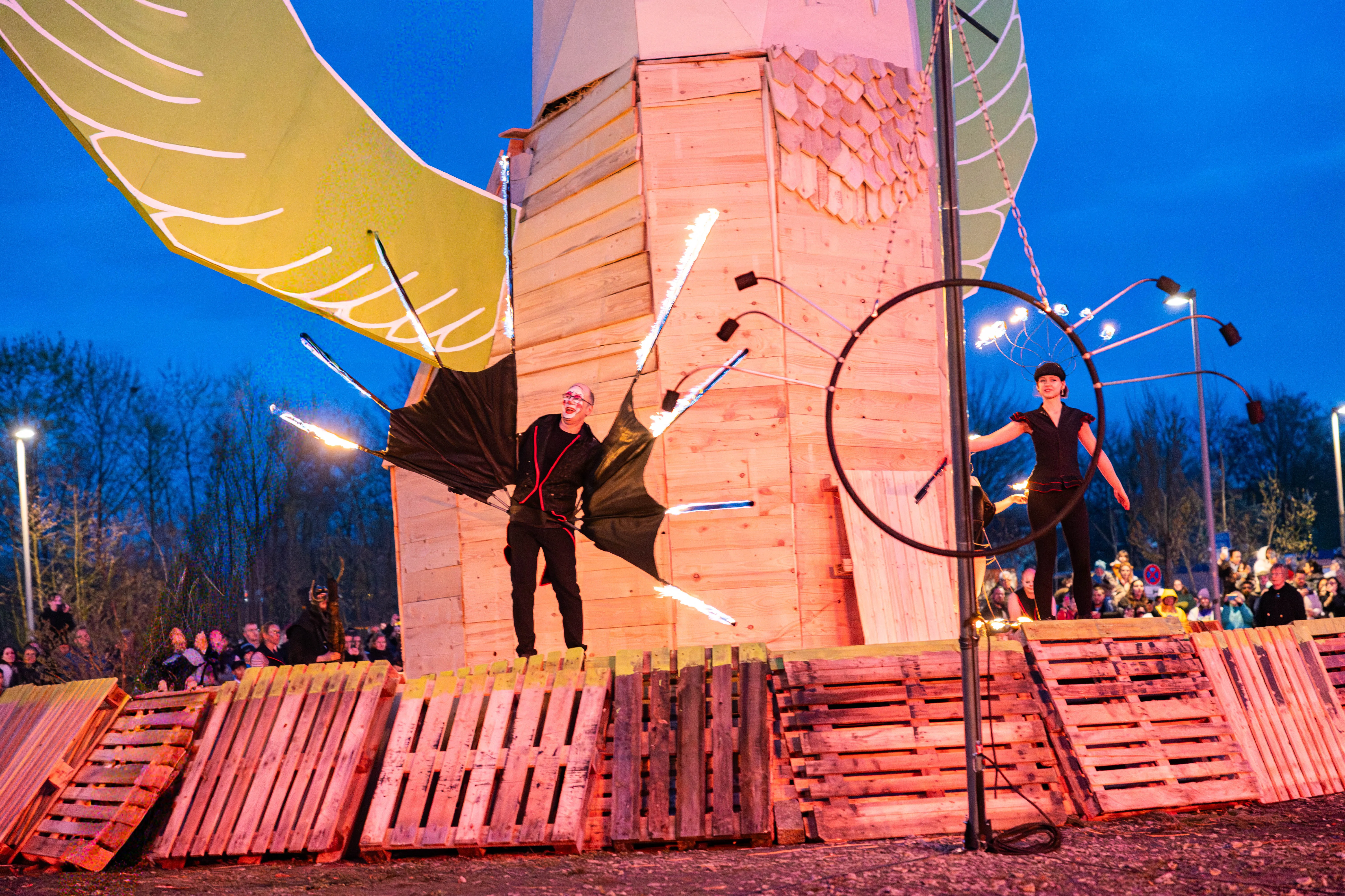 Zwei Artisten treten vor Publikum bei der Osterfeuer-Veranstaltung „Burn the Fox“ in Lüdenscheid auf. Ein Künstler mit Flügeln jongliert mit brennenden Keulen, während eine andere Person in einem Reifen balanciert.