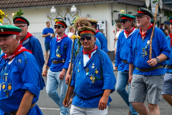 Mitglieder der Meinerzhagener Schützengilde in blauen Hemden und roten Halstüchern gehen in einer Gruppe durch eine Straße.