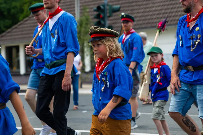 Mitglieder der Meinerzhagener Schützengilde in blauen Hemden und roten Halstüchern ziehen in einer Prozession durch die Straße.