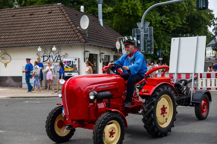 Stefan Schneider fährt einen kleinen roten Traktor mit Anhänger auf einer Straße.
