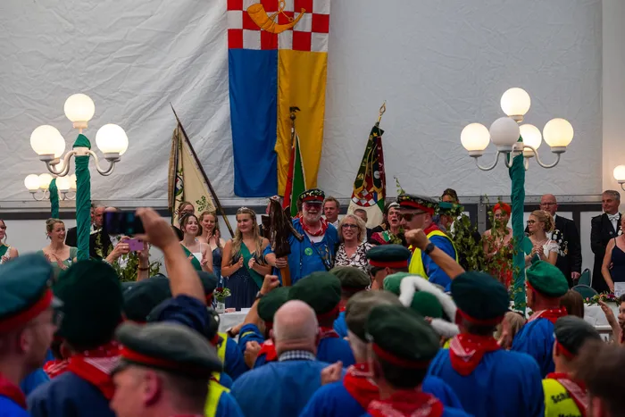 Stefan Schneider wird im Kreise von Mitgliedern der Meinerzhagener Schützengilde in blauen Uniformen und festlicher Kleidung vor großen Fahnen gefeiert.