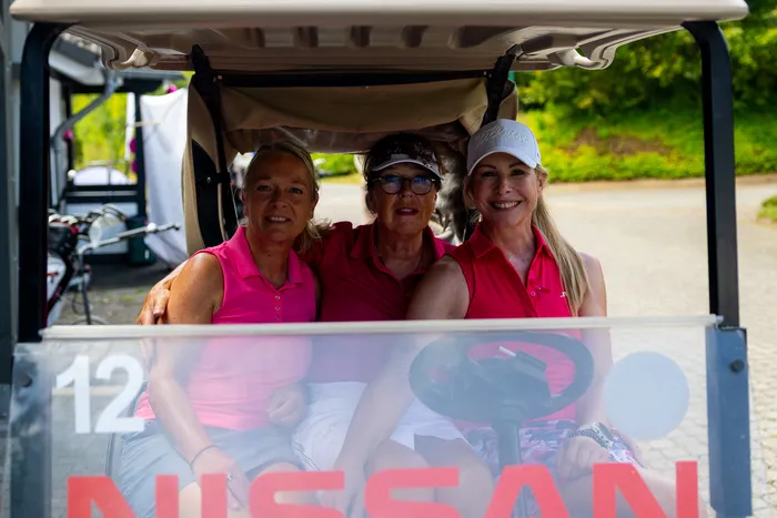 Drei Frauen in pinken und roten Poloshirts sitzen in einem Golfkarren.