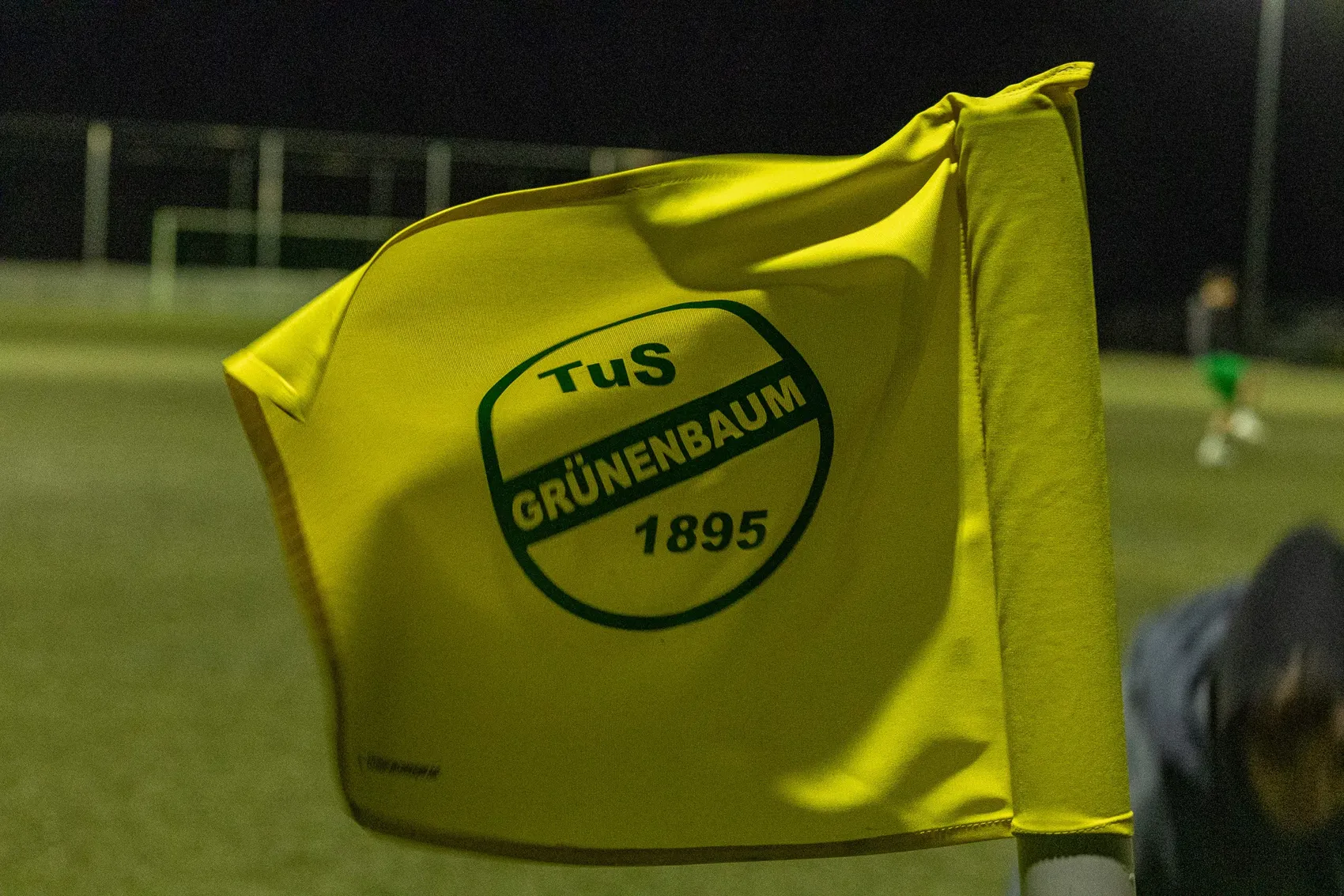 Gelbe Flagge mit dem grünen Vereinslogo des TuS Grünenbaum und der Gründungszahl 1895 weht im Wind.