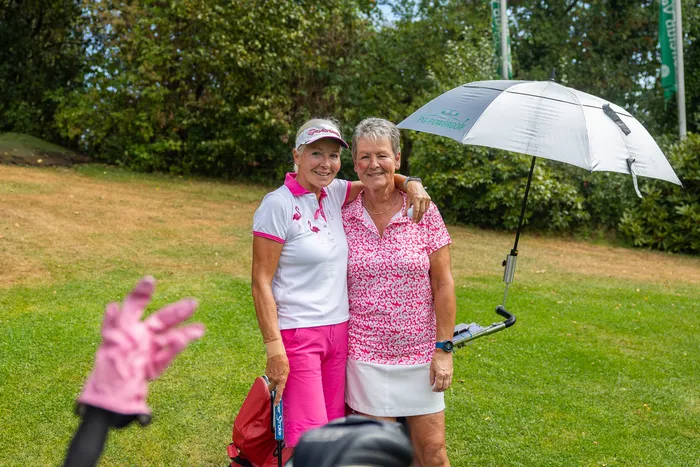 Zwei Frauen in Golfbekleidung mit pinkfarbenen Akzenten stehen auf einem Rasen und lächeln.