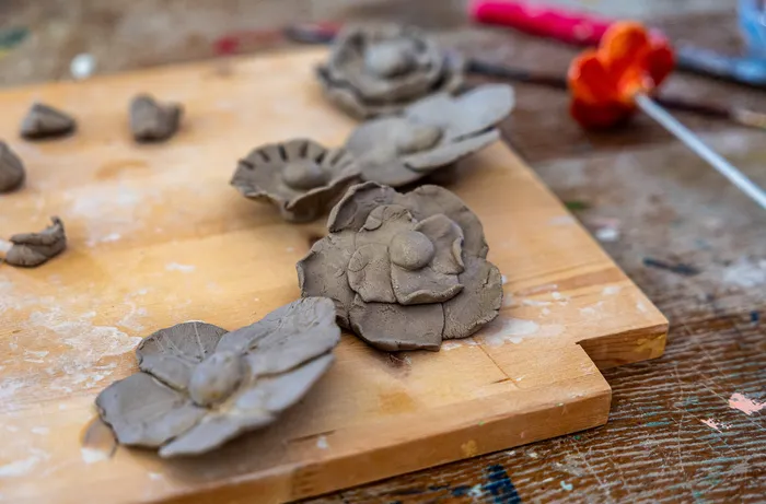 Handgeformte Blumen aus Ton liegen auf einem Holzbrett.