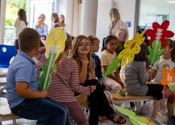 Kinder halten große, bunte Papierblumen als Requisiten für ihr Theaterstück in der Regenbogenschule.
